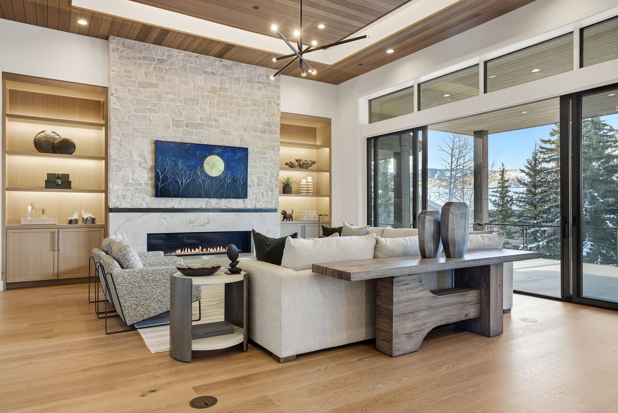 Spacious living area featuring a stone-clad fireplace with a linear insert, built-in shelving with integrated lighting, wood-finish flooring, a wood-paneled ceiling, and large sliding glass doors leading to an outdoor space