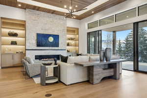 Spacious living area featuring a stone-clad fireplace with a linear insert, built-in shelving with integrated lighting, wood-finish flooring, a wood-paneled ceiling, and large sliding glass doors leading to an outdoor space