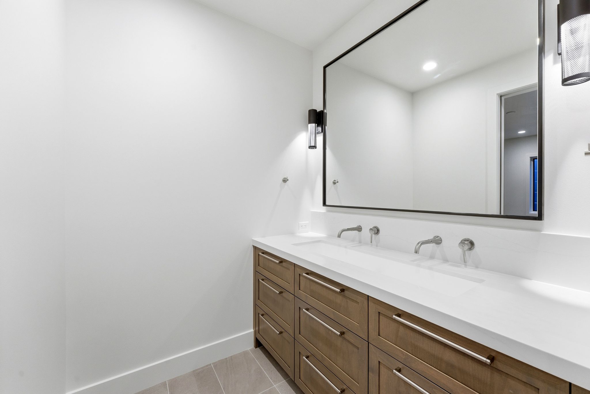 Dual sink vanity featuring a white countertop, wall-mounted faucets, and wood-finish cabinetry with silver hardware