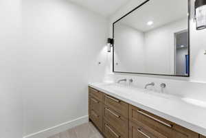 Dual sink vanity featuring a white countertop, wall-mounted faucets, and wood-finish cabinetry with silver hardware