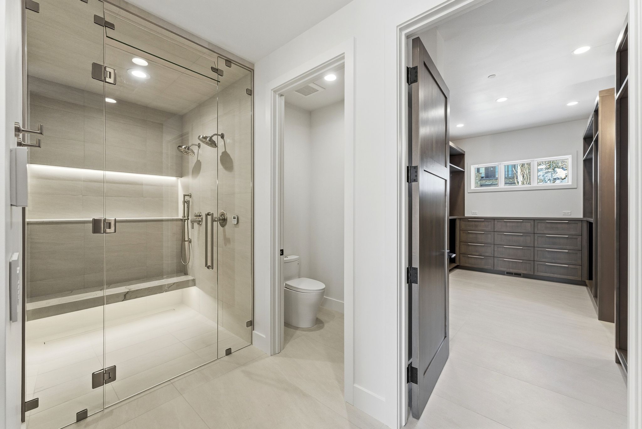 Glass-enclosed shower with a built-in bench, dual shower heads, and an integrated illuminated niche