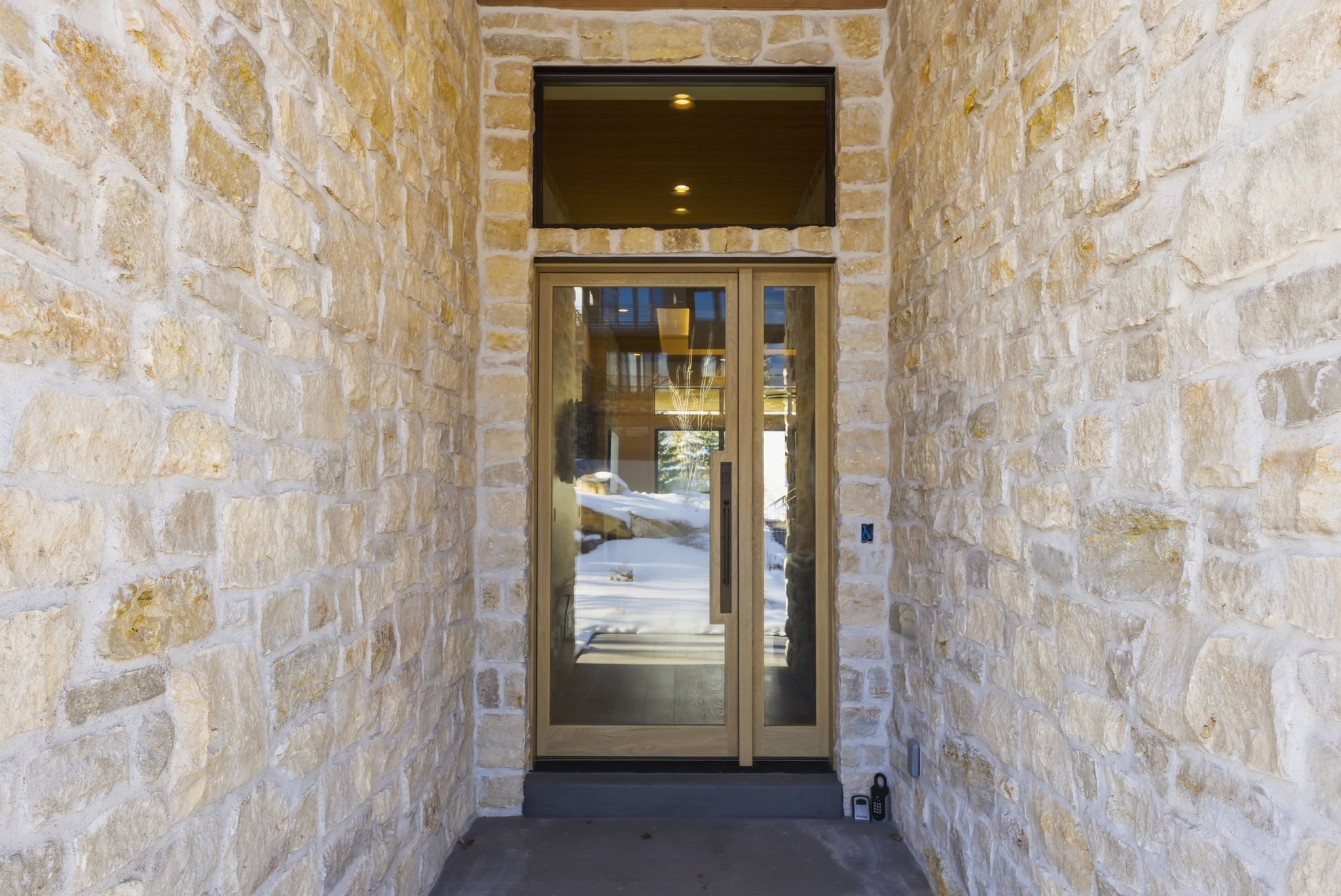 Stone veneer exterior facade with a wood-framed glass entry door and transom window