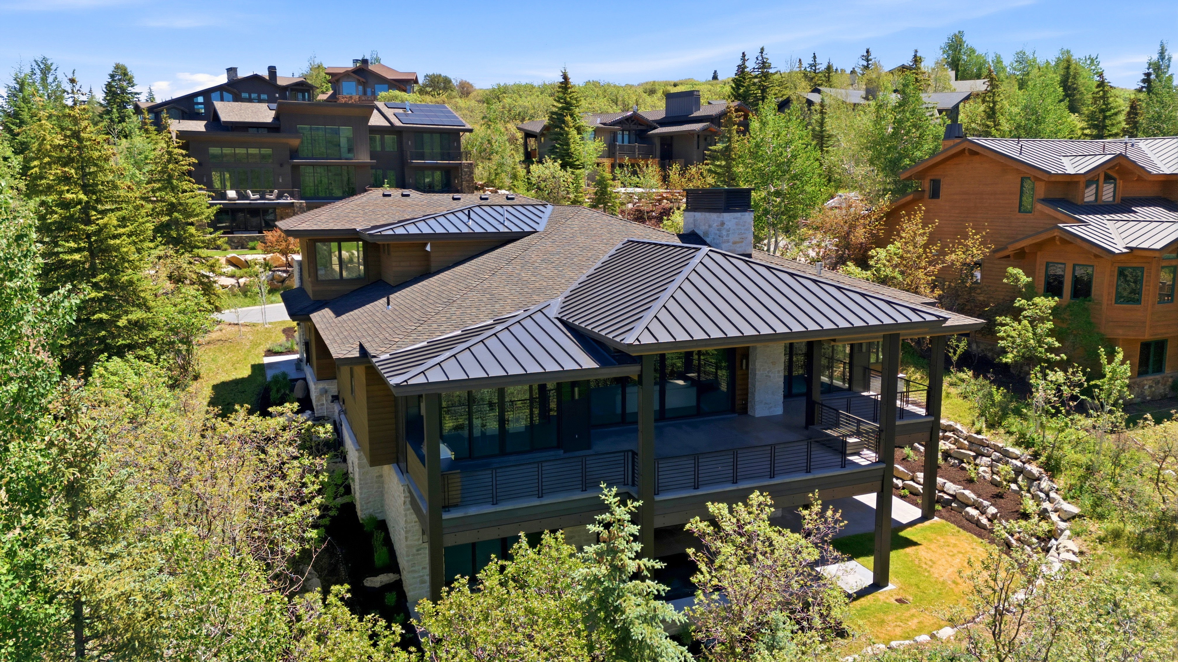 Modern home with a stone and wood siding exterior, featuring a metal roof section and a covered deck