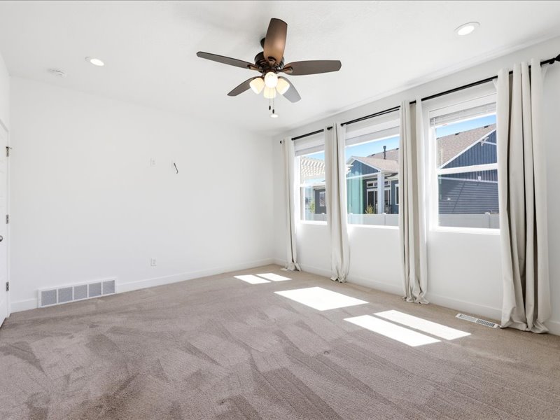 Spacious room featuring plush carpet flooring, a ceiling fan with integrated lighting, recessed lighting, and three large windows with curtain rods and drapes