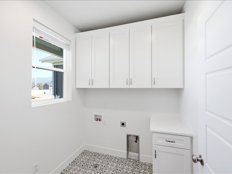 Dedicated laundry space featuring white cabinetry with brushed nickel hardware, a single window, patterned floor tile, and a built-in counter with additional storage