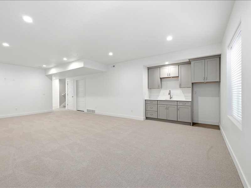Spacious carpeted room featuring a wet bar with gray cabinetry, white subway tile backsplash, and a stainless steel faucet