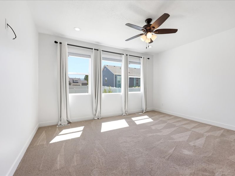 Bright room featuring three large windows, neutral carpet, a ceiling fan with integrated lighting, recessed lighting, and white walls