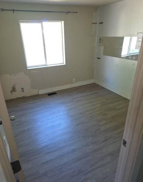 Room featuring wood-finish flooring, a window with natural light, neutral wall tones, and white baseboards