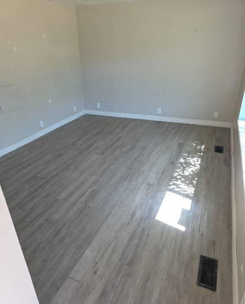 Spacious room featuring wood-finish flooring, light-toned walls, and white baseboards