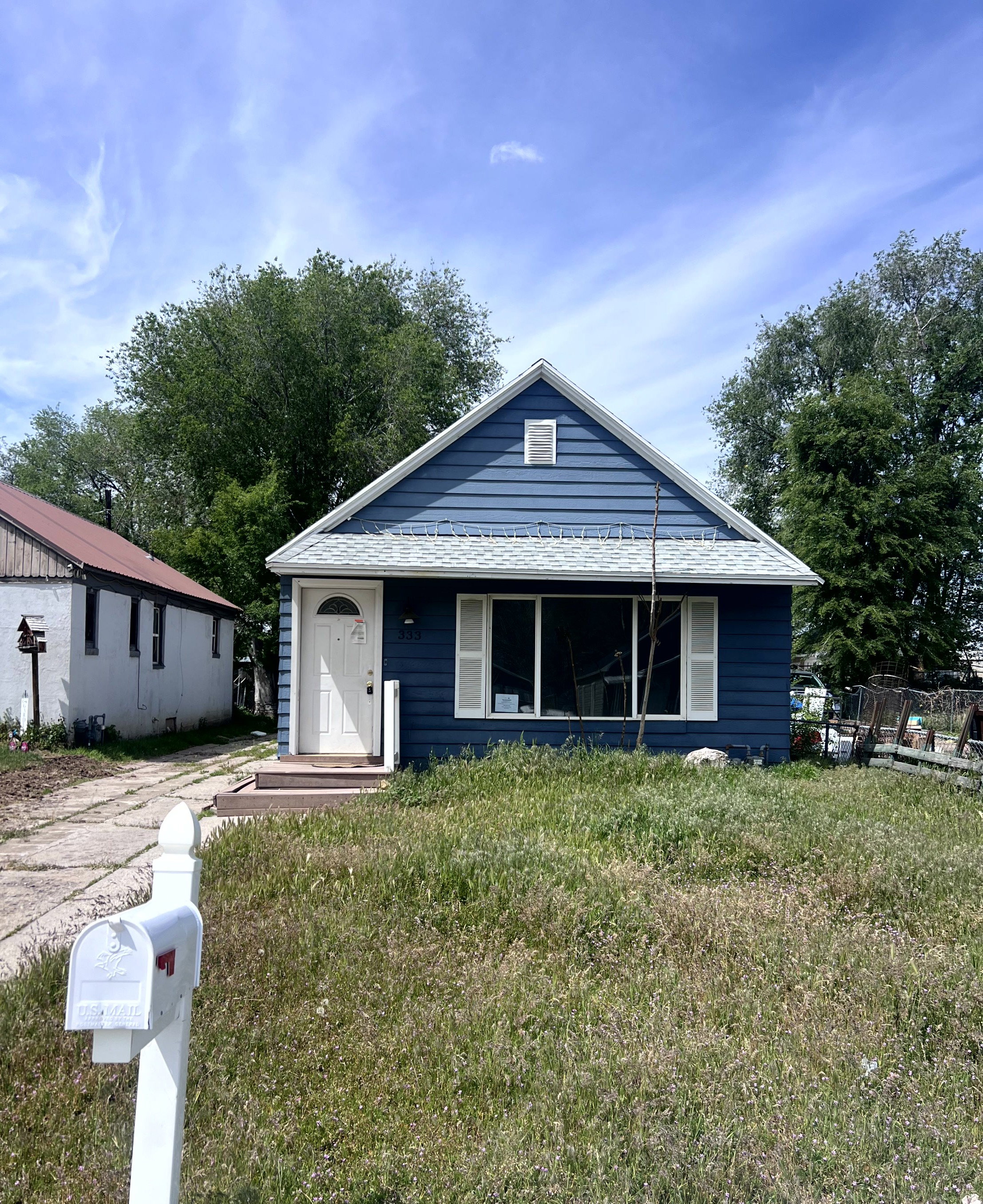 Blue horizontal siding, white gable trim, white front door with arched window, large front window with white shutters, and a white shingle roof