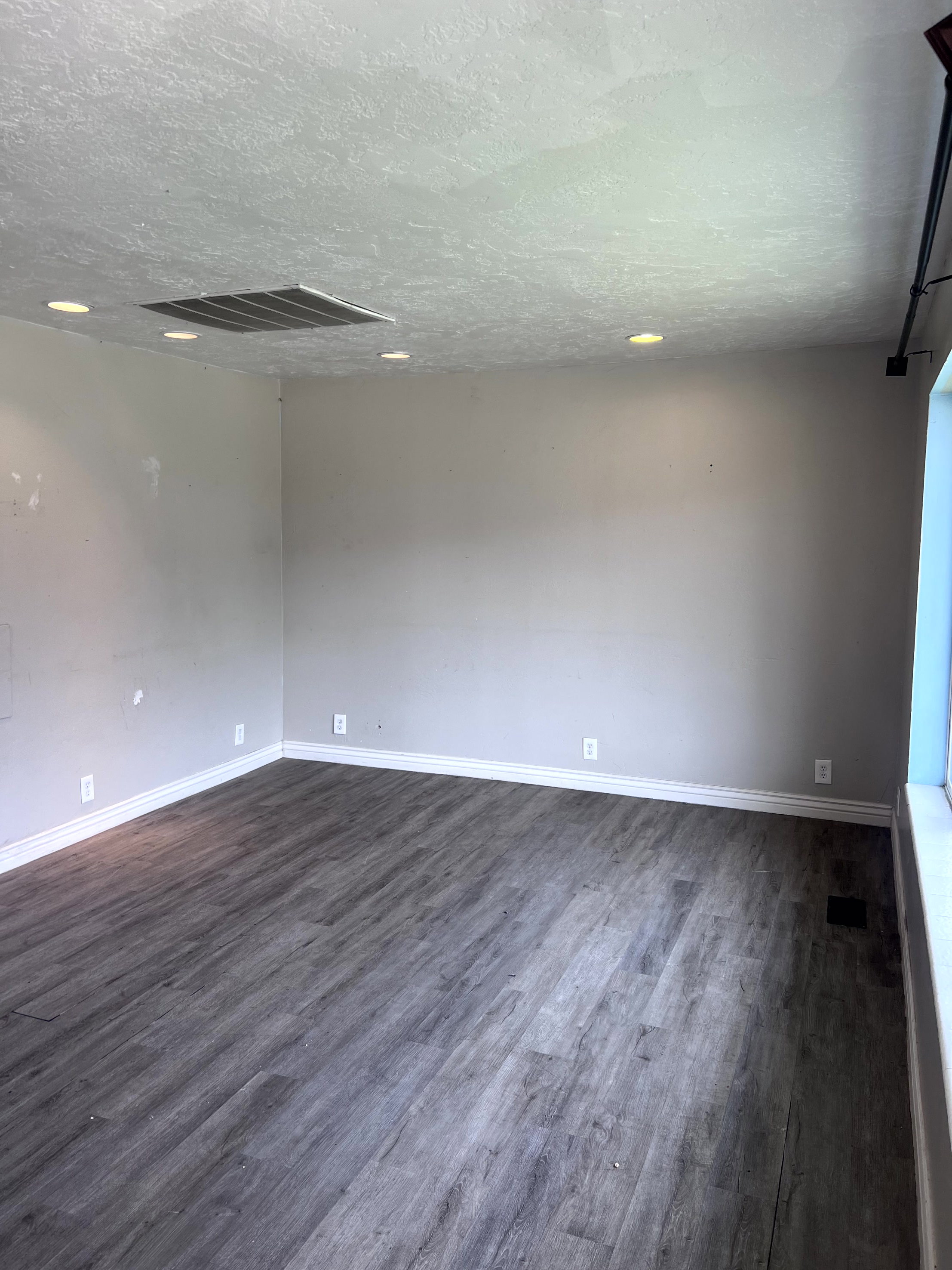 Spacious room featuring wood-finish flooring, light grey walls, white baseboards, and recessed ceiling lighting