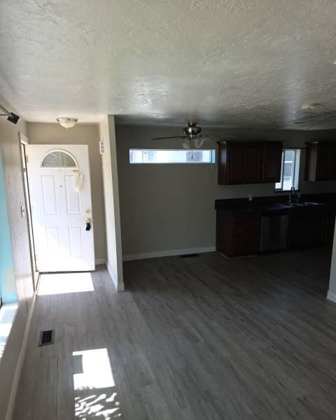Open-concept living space with wood-finish flooring, a contemporary ceiling fan, and a transom window providing natural light