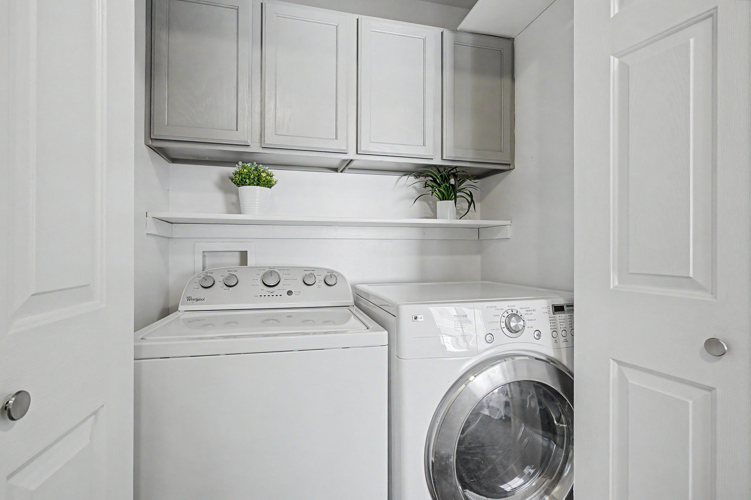 Dedicated laundry closet featuring a top-load washer, front-load dryer, and upper cabinetry with integrated shelving