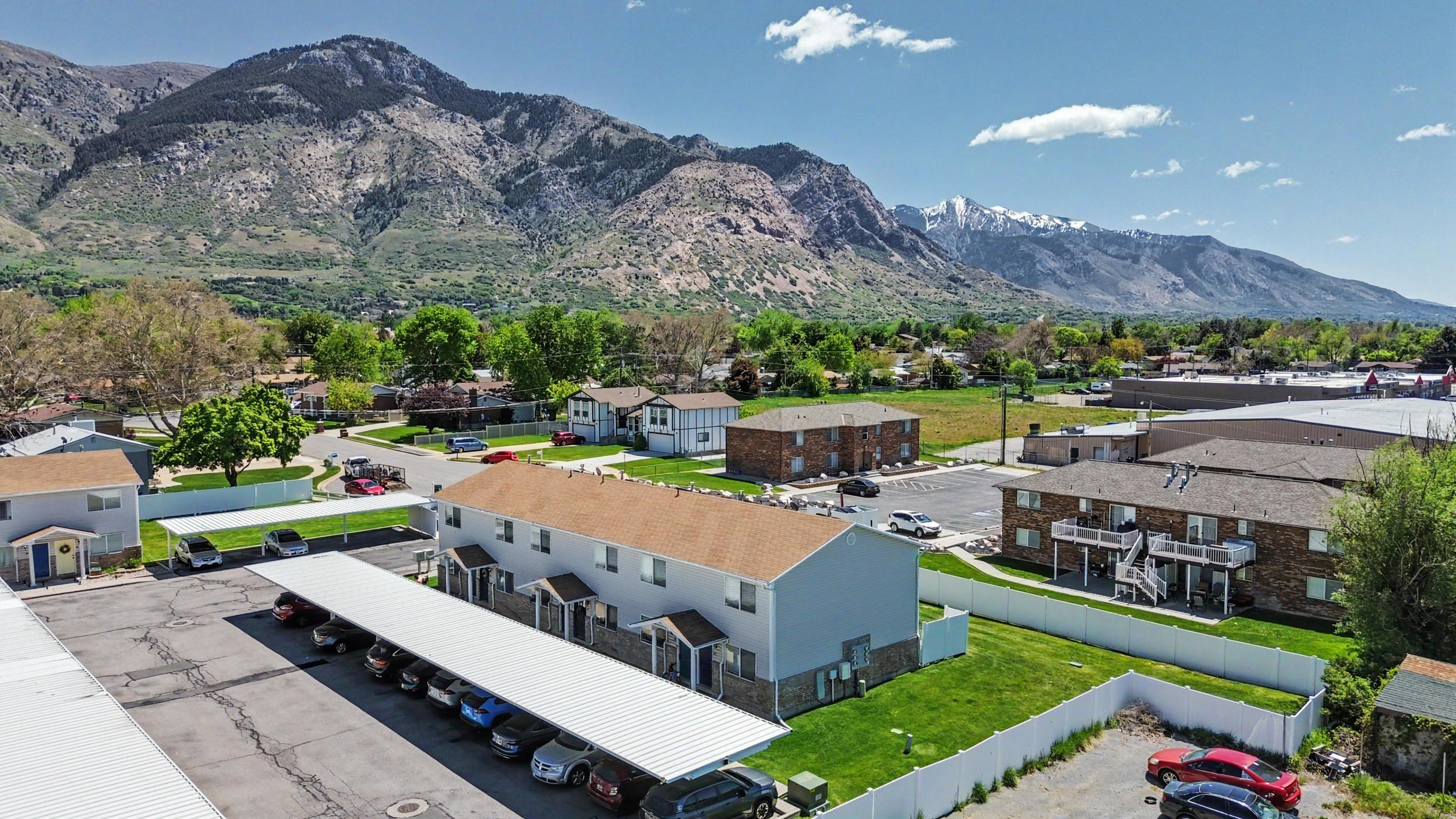 Expansive property featuring multiple residential buildings with tan shingle roofs, covered parking structures, and green lawns