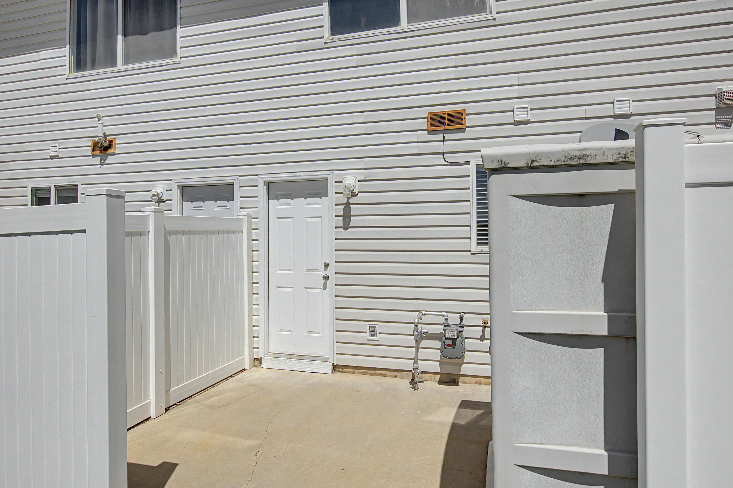 Rear exterior featuring white vinyl siding, a private concrete patio, and a white paneled privacy fence