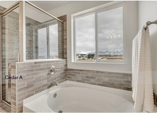 Soaking tub with a tiled surround, featuring a large window and an adjacent glass-enclosed shower. These pictures are of another home.