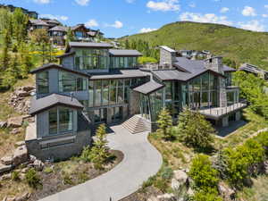 Contemporary multi-level residence featuring extensive floor-to-ceiling windows, stone and horizontal siding exterior, multiple outdoor deck spaces, a paved driveway, and natural rock landscaping