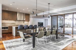 Open-concept living area featuring rich wood-finish flooring, a modern kitchen with integrated appliances, a spacious island with seating, a large dining area, and expansive sliding glass doors