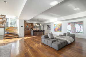 Spacious open-concept interior featuring hardwood flooring, a built-in wet bar with seating, a contemporary staircase with metal railings, recessed lighting, and expansive wall space for art