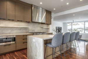 Gourmet kitchen featuring wood-finish cabinetry, stainless steel appliances, a range hood, and an oversized island with a waterfall countertop