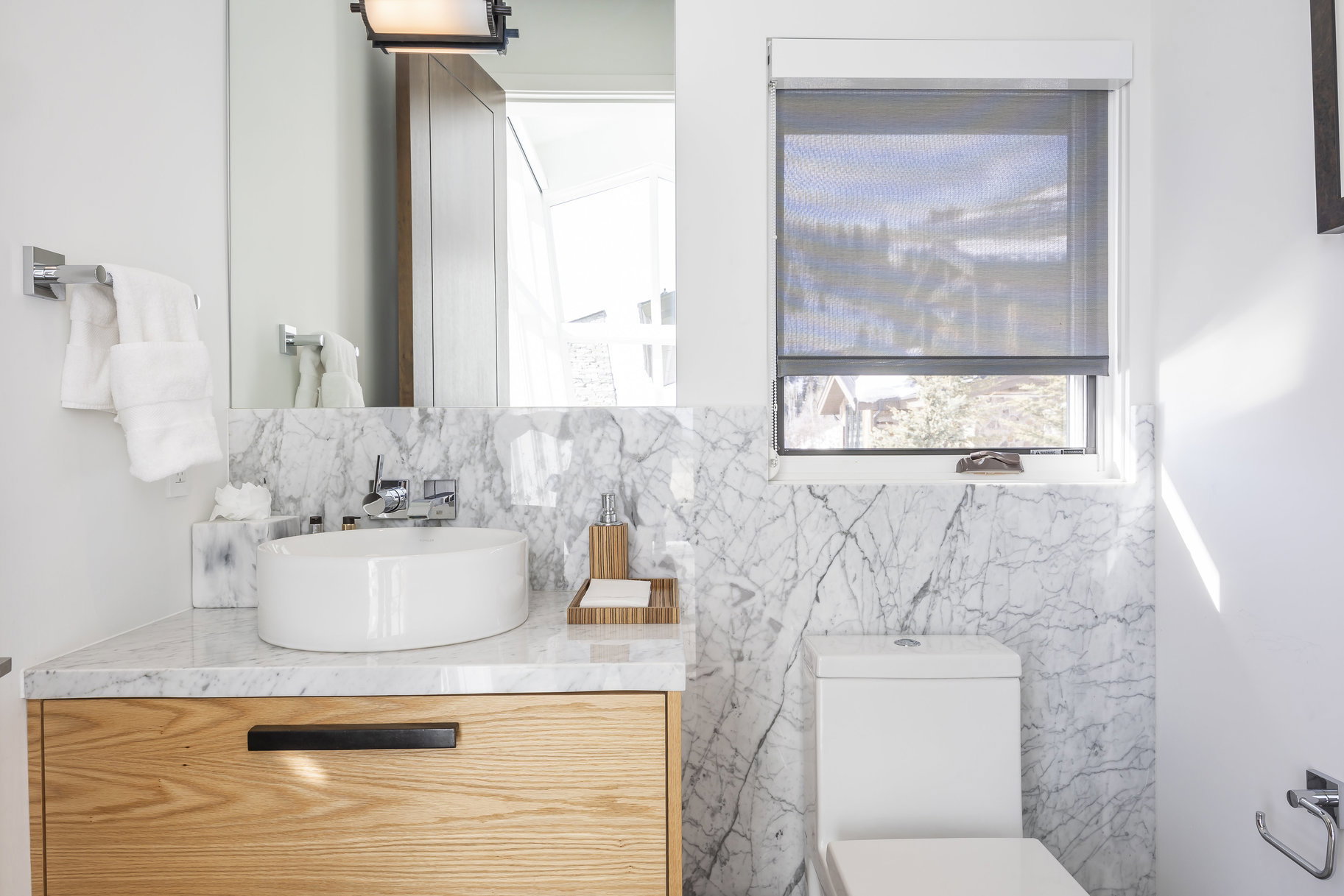 Modern bathroom featuring a wood-finish floating vanity with a white vessel sink, polished chrome faucet, and white marble countertop and backsplash