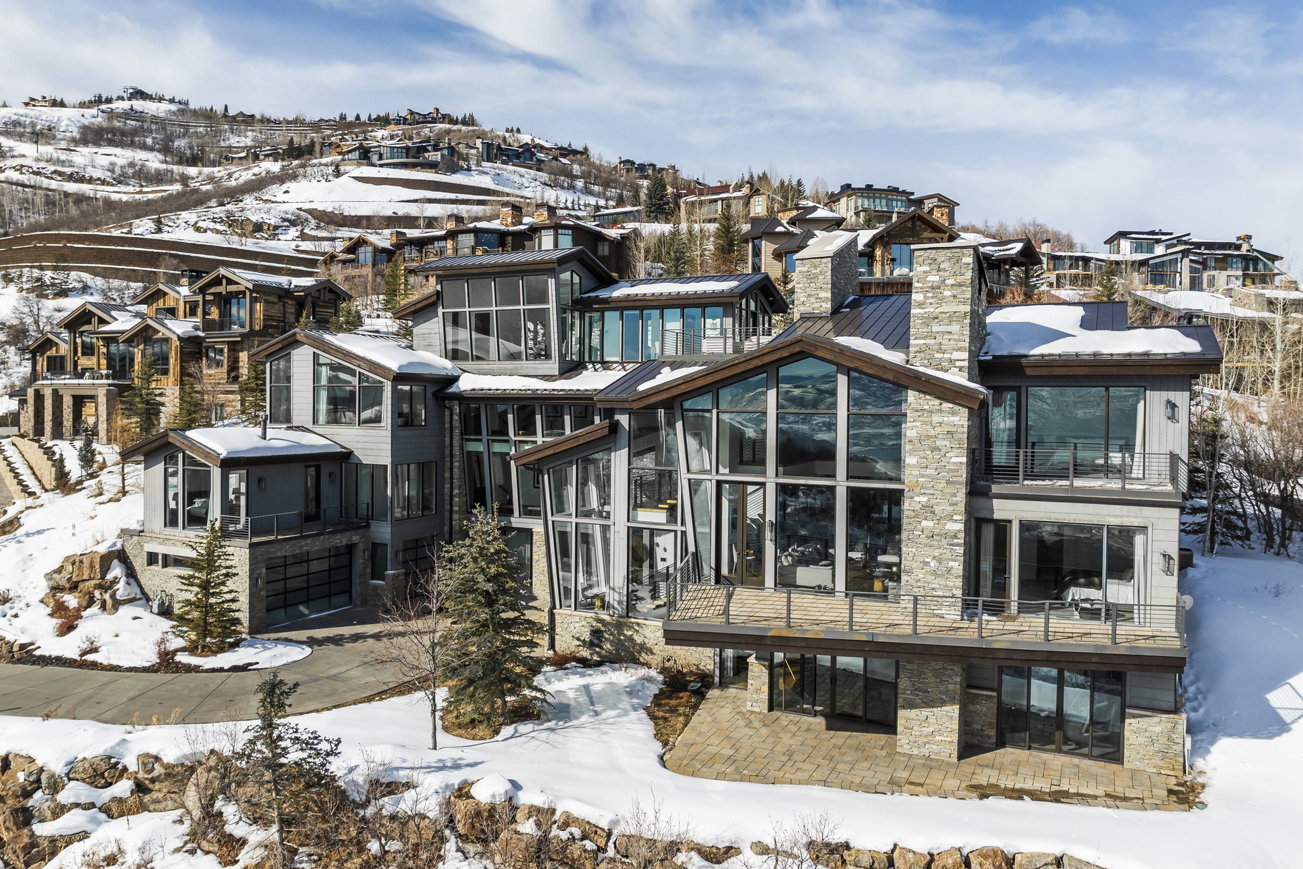 Contemporary mountain dwelling featuring expansive windows, multiple balconies, a stone-clad chimney, and a multi-level architectural design