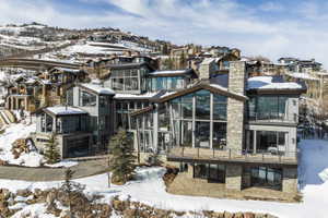 Contemporary mountain dwelling featuring expansive windows, multiple balconies, a stone-clad chimney, and a multi-level architectural design