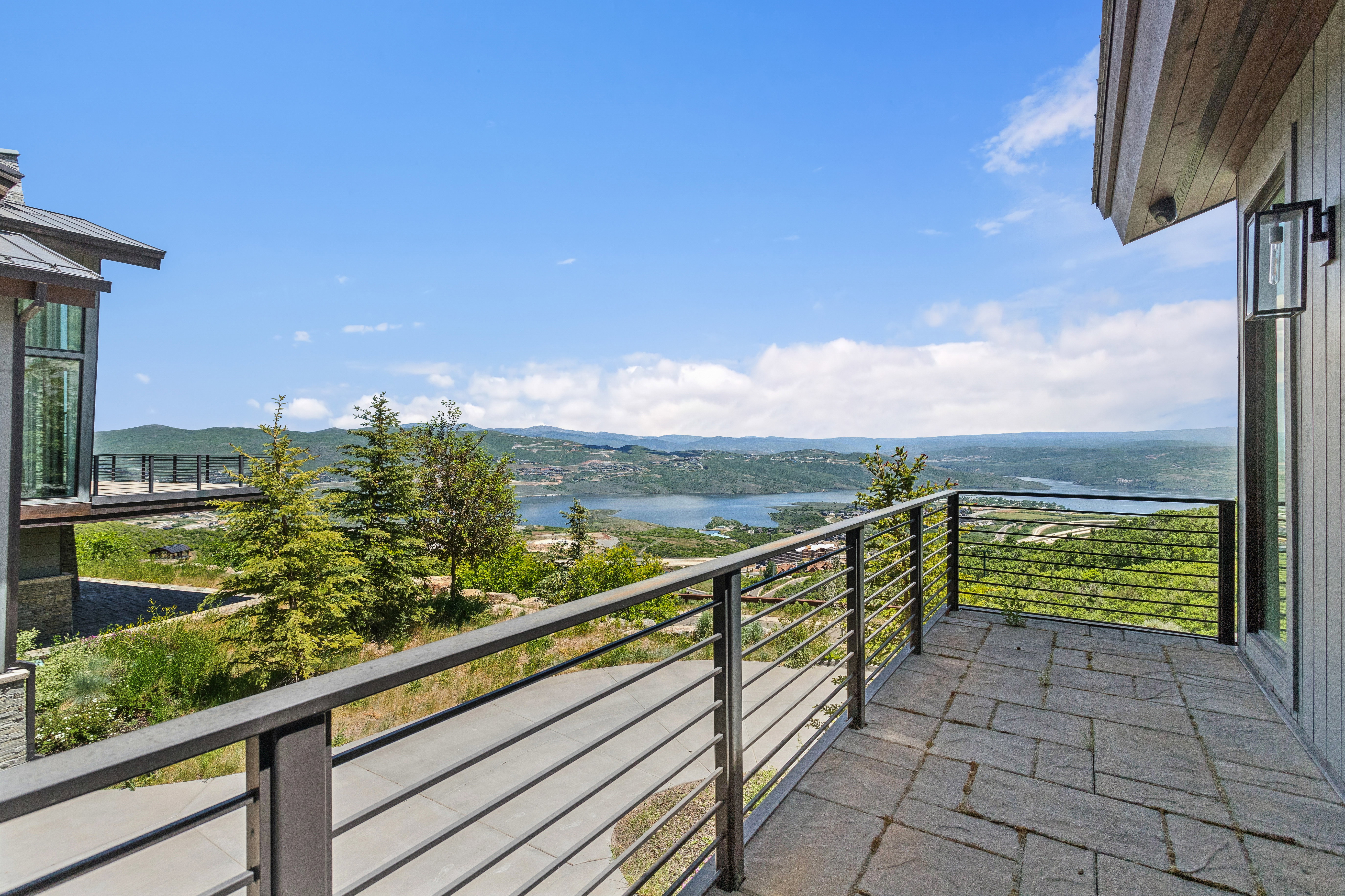 Outdoor patio featuring stone tile flooring, modern metal railing, and expansive water and mountain scenery