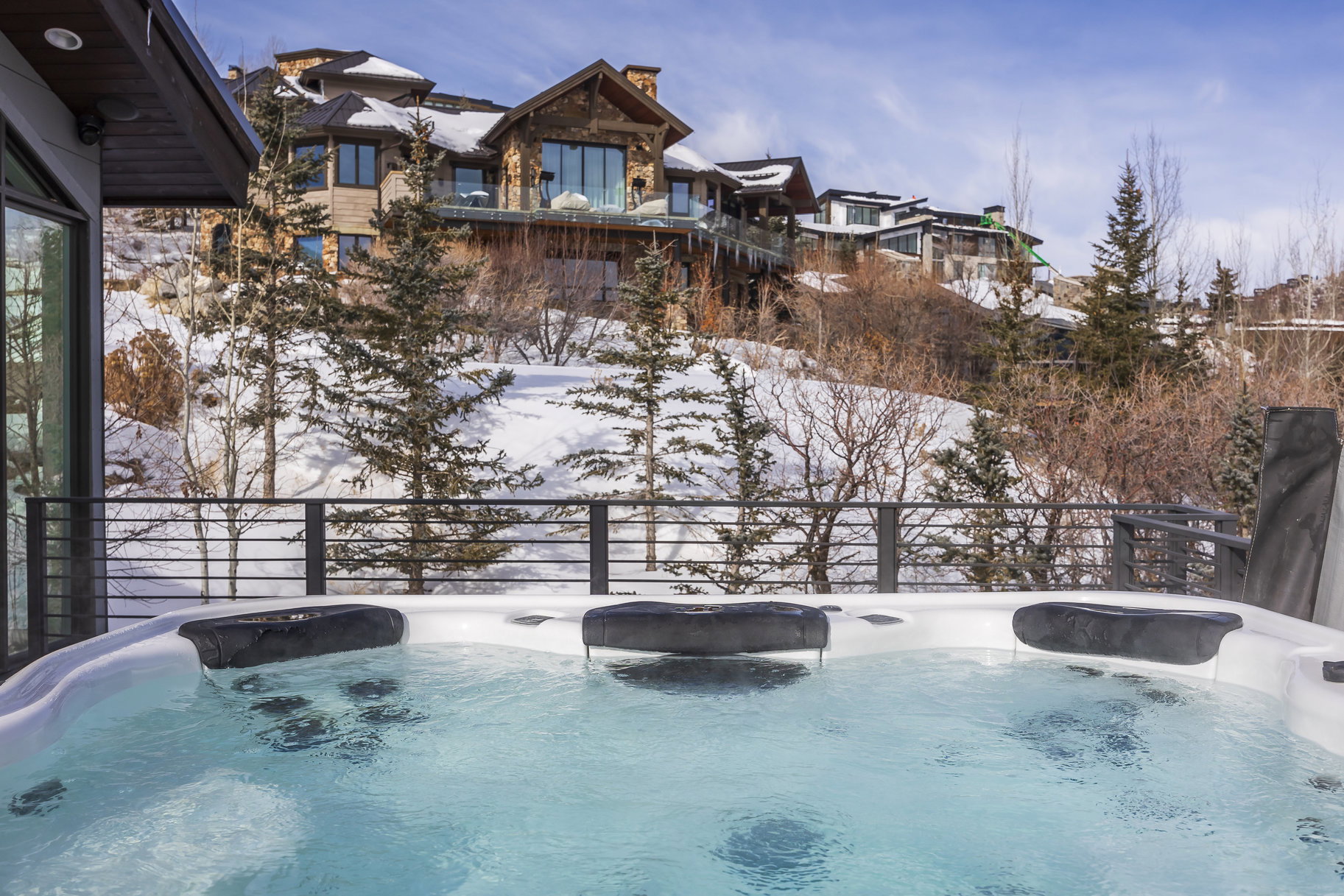 Deck-mounted hot tub featuring integrated headrests and a black metal railing