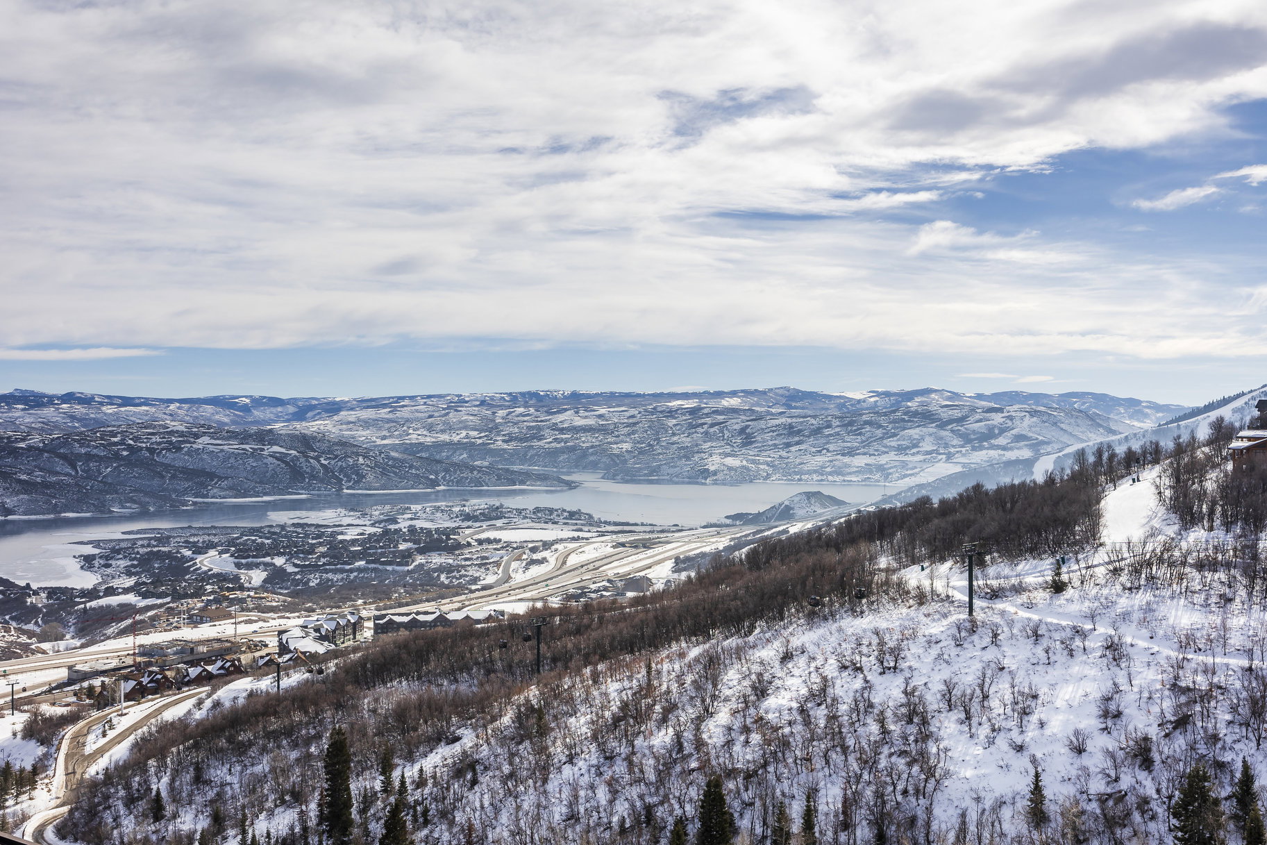 Expansive mountain landscape featuring snow-covered terrain, a large body of water, and distant mountain ranges