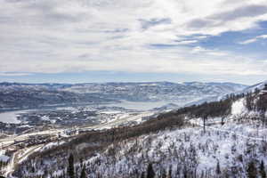 Expansive mountain landscape featuring snow-covered terrain, a large body of water, and distant mountain ranges