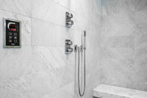 Shower featuring large format white marble-finish wall tiles, chrome fixtures, and a built-in bench
