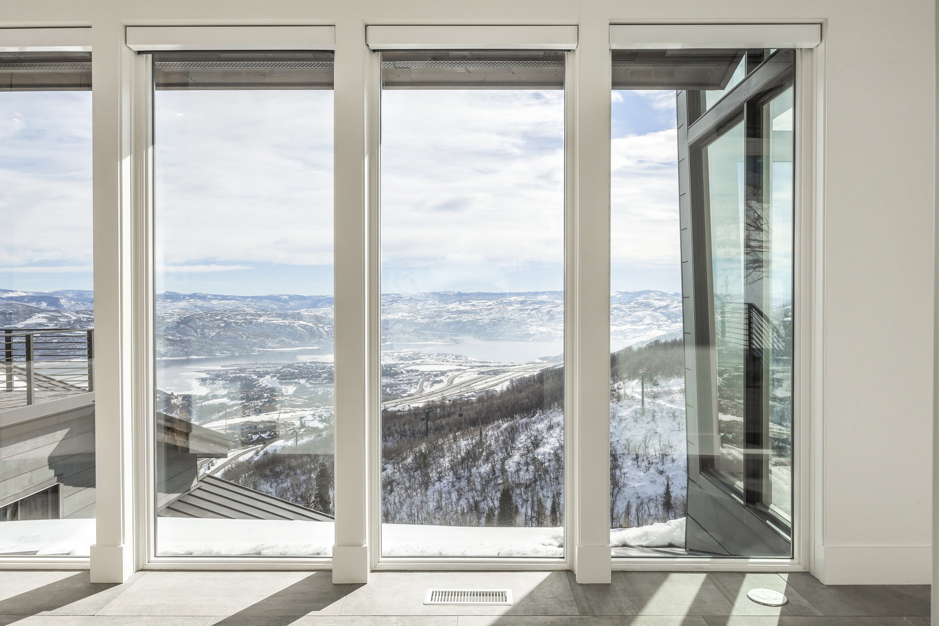 Floor-to-ceiling windows with roller shades framing a snowy mountain landscape and distant body of water