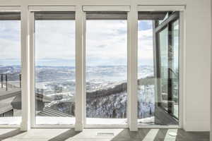 Floor-to-ceiling windows with roller shades framing a snowy mountain landscape and distant body of water