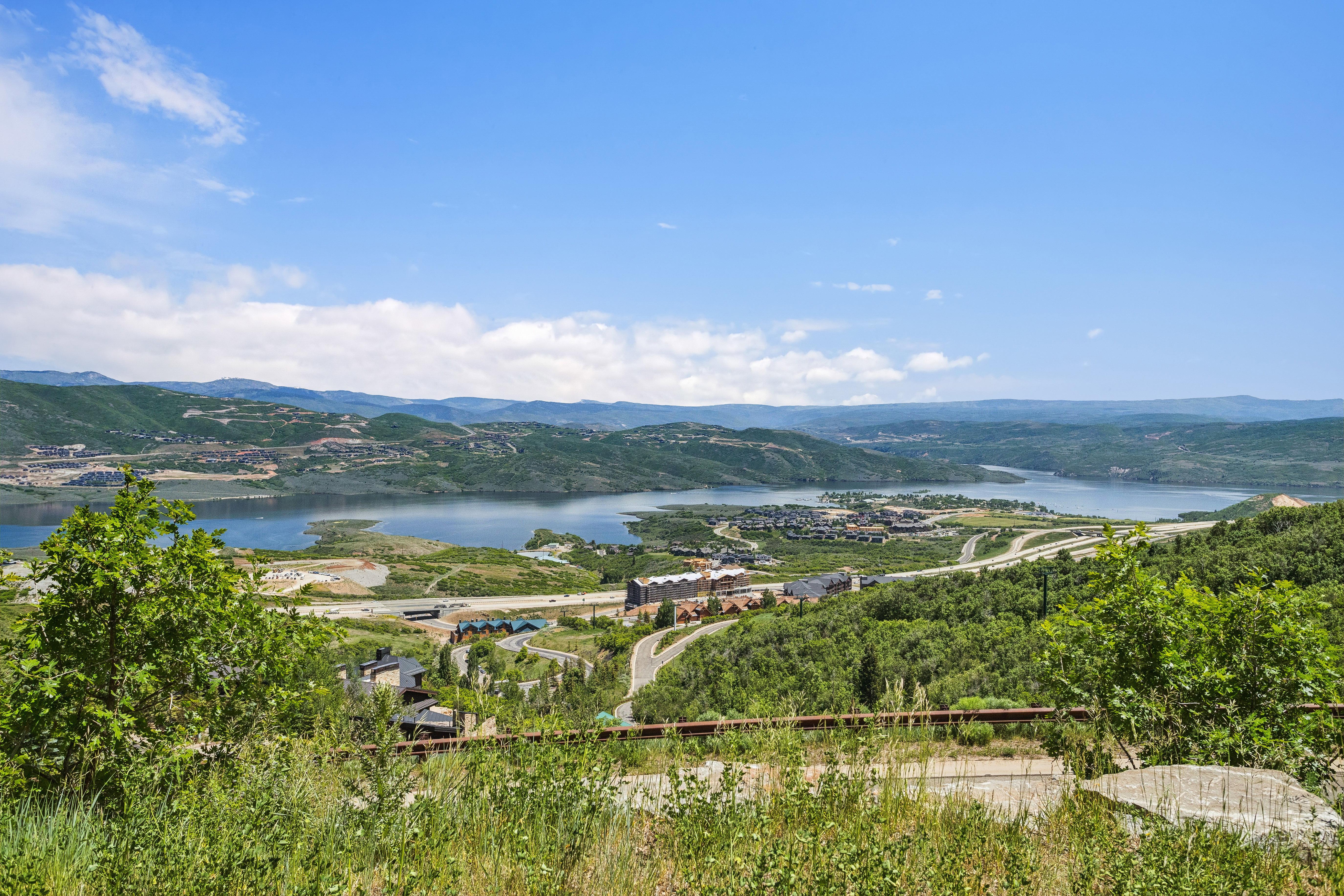 Expansive mountain and lake scenery featuring distant residential development and lush green hillsides