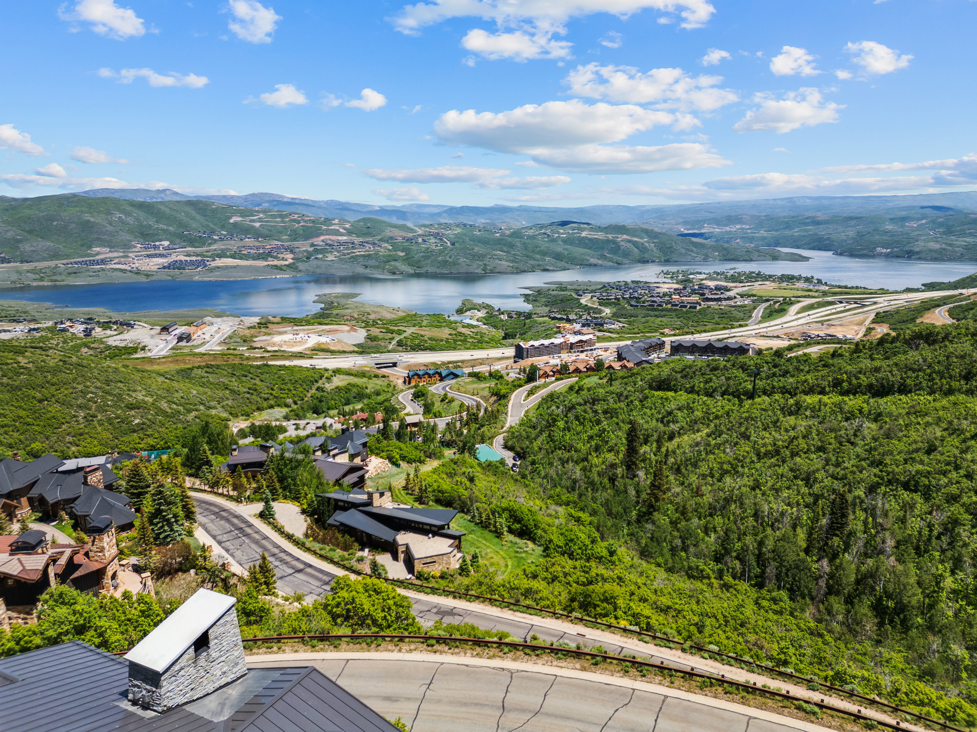 Expansive mountain landscape featuring a large body of water, extensive tree cover, and distant residential developments