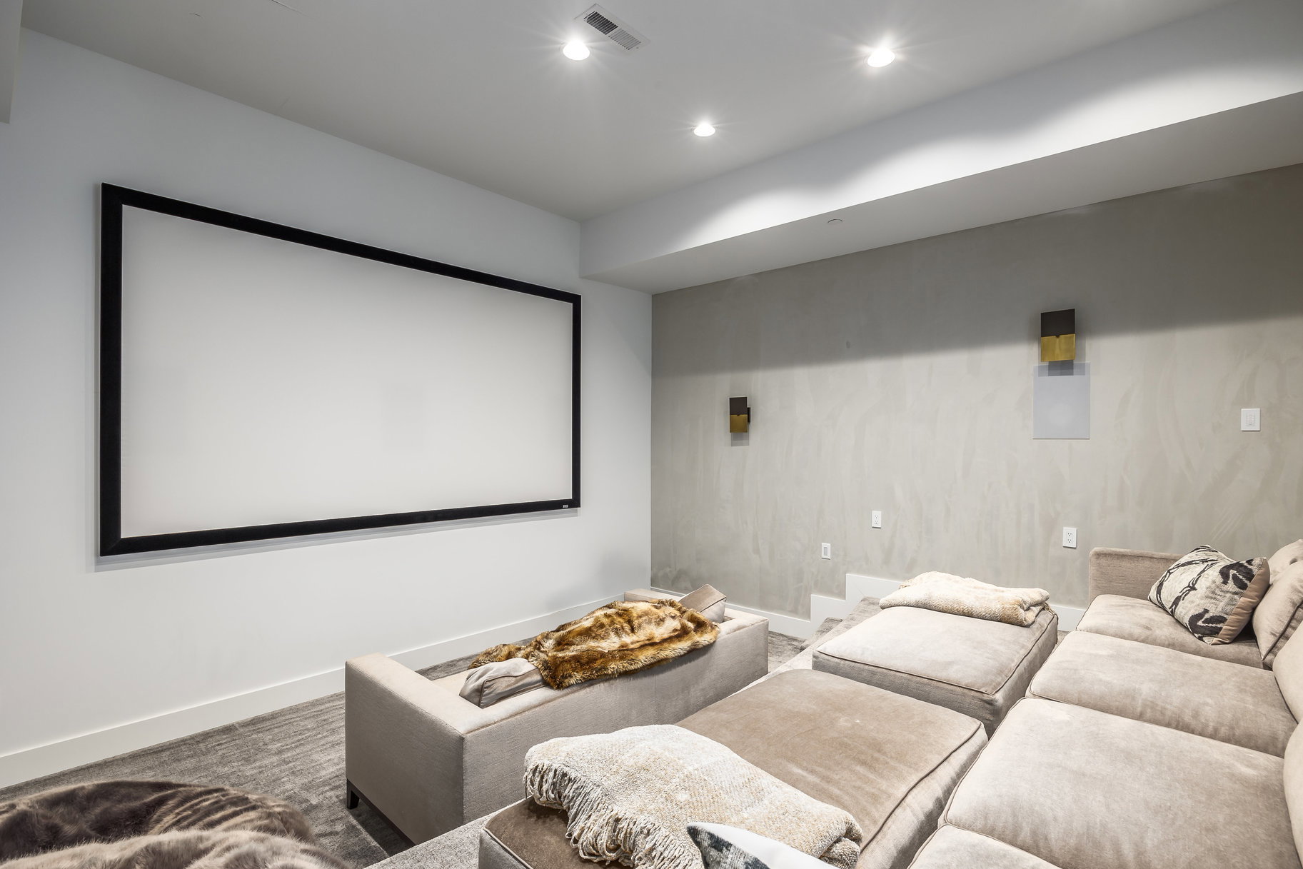 Dedicated media room featuring a large projection screen, recessed lighting, wall-mounted speakers, and a textured accent wall