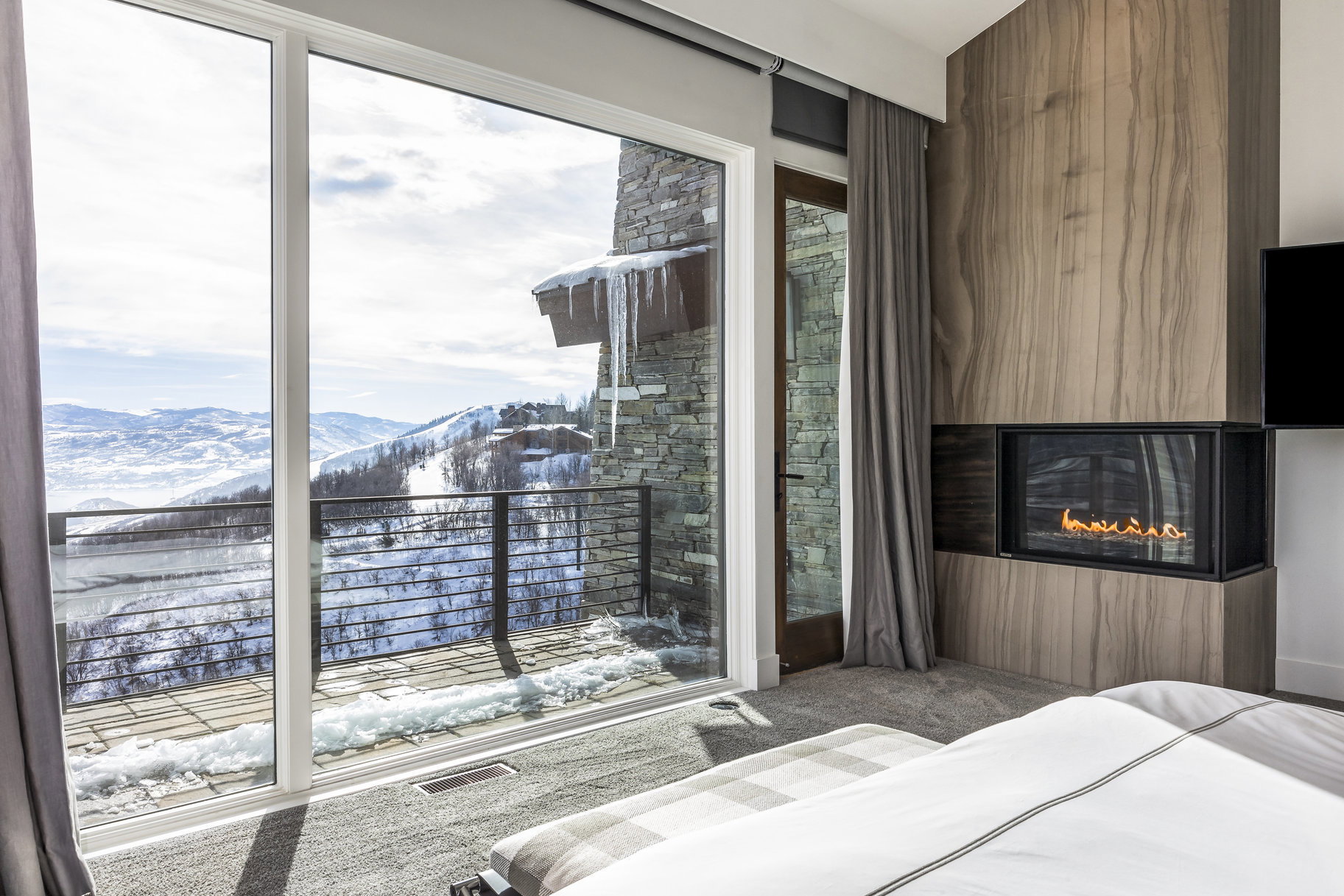 Full-height sliding glass doors opening to an outdoor balcony with metal railings and mountain scenery
