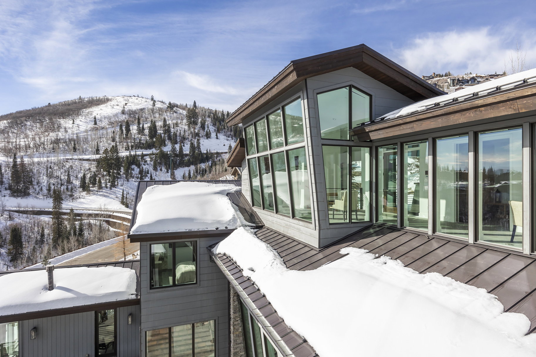 Modern architectural design featuring expansive window walls, a metal roof, and a backdrop of snow-covered mountains