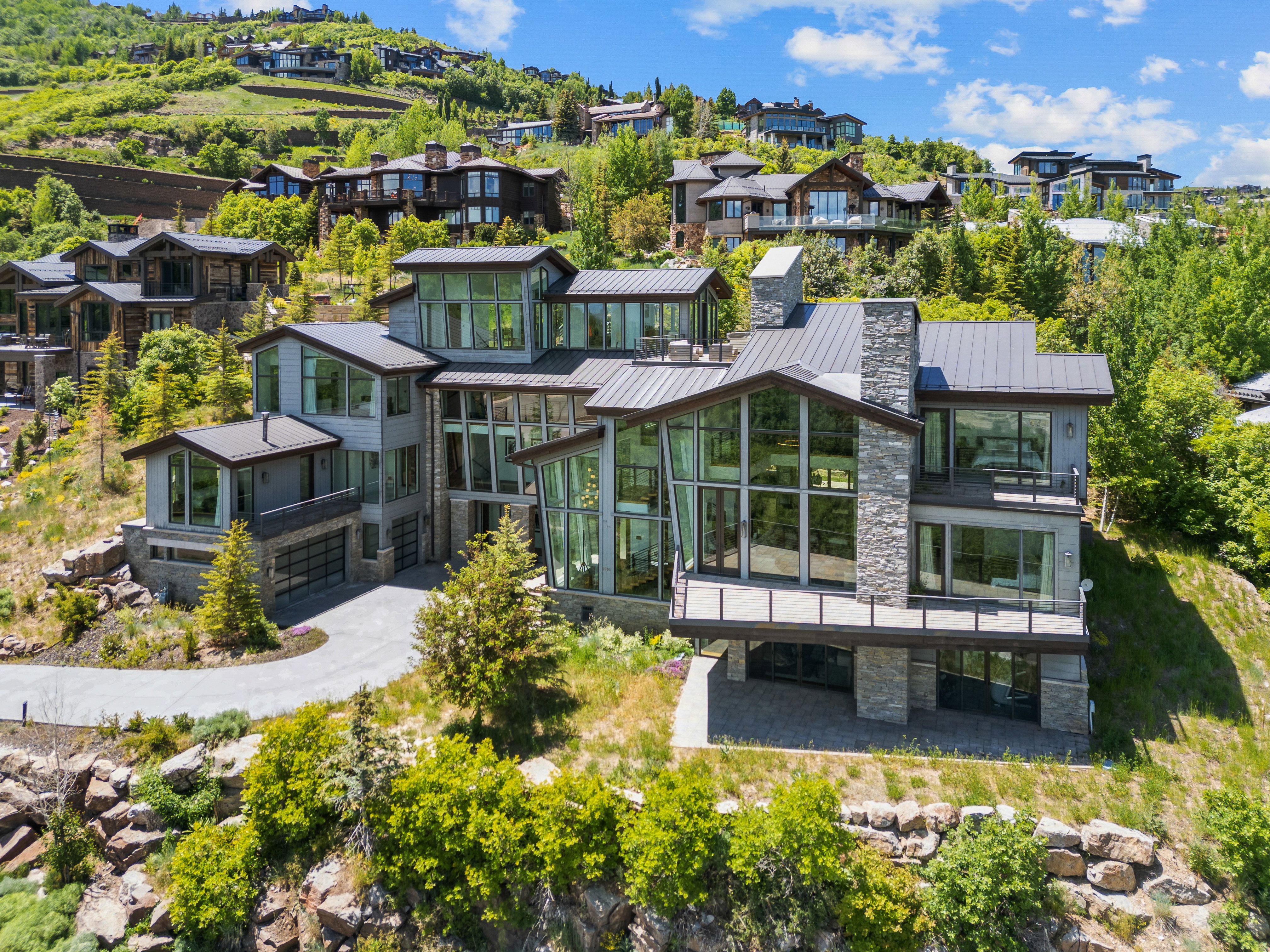 Contemporary multi-level residence featuring expansive windows, stone and siding exterior elements, and multiple balconies