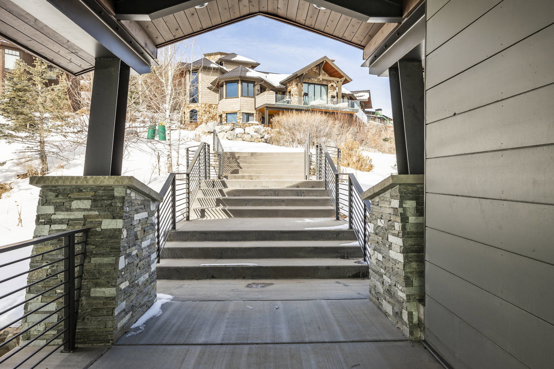 Grand exterior stairway featuring horizontal railings and stone-clad pillars, leading to an upper residence with multiple windows