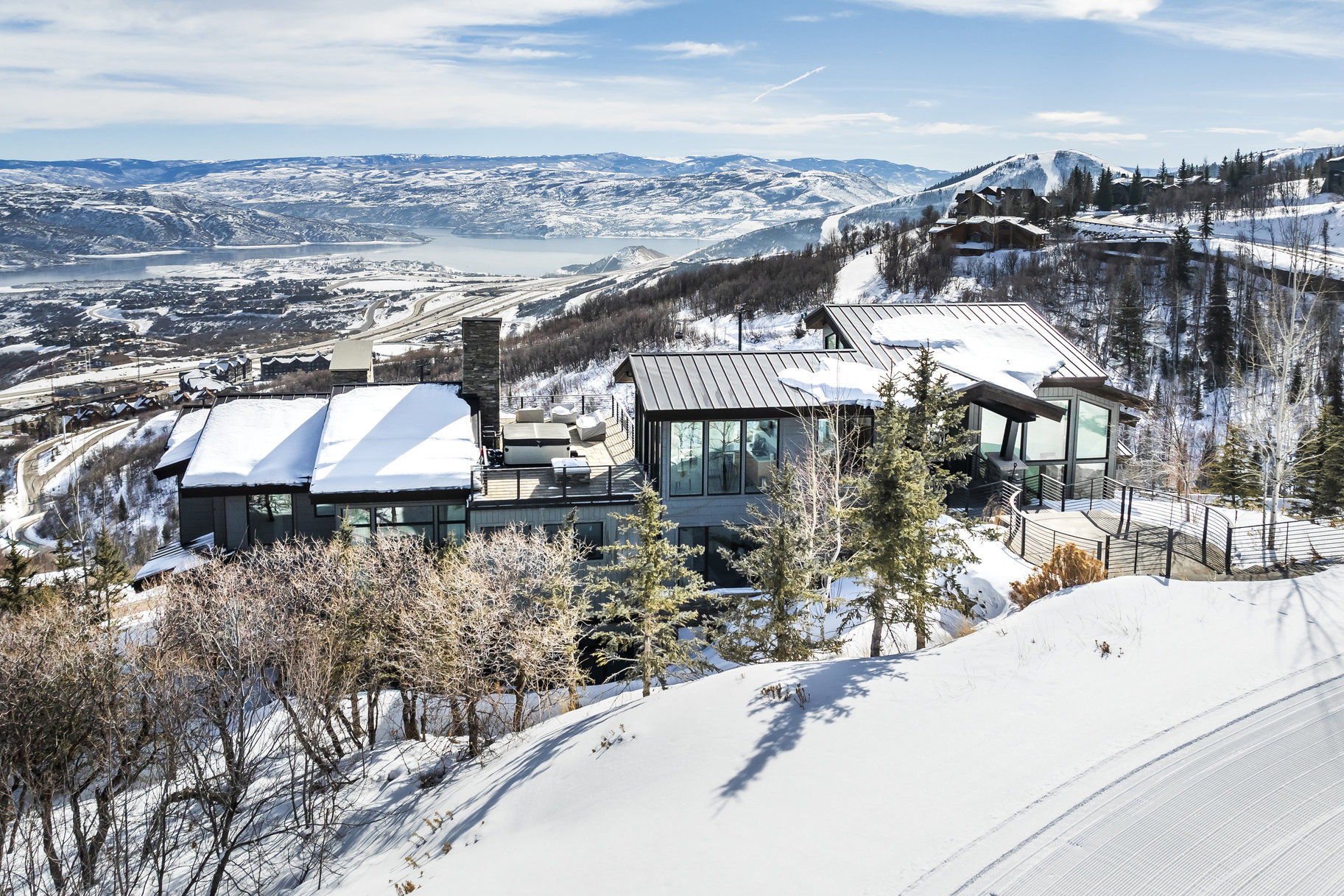 Modern architecture featuring expansive windows, multiple outdoor terrace spaces, a stone chimney, and a metal roof