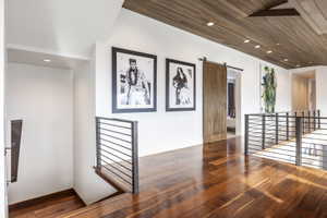 Hardwood flooring throughout a bright hallway featuring a wood-panel ceiling with recessed lighting