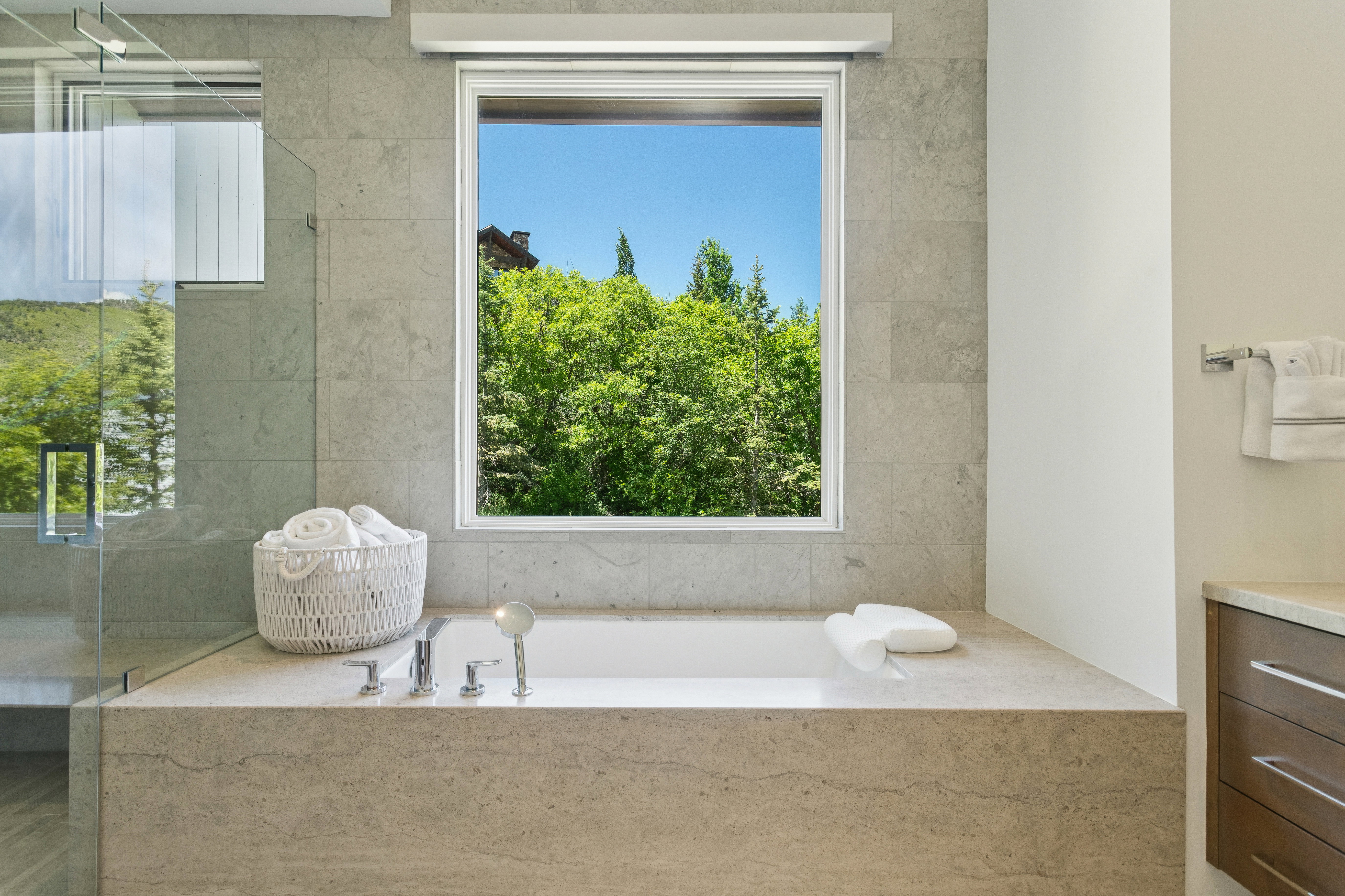 Bathroom featuring a built-in soaking tub with deck-mounted fixtures, a glass-enclosed shower, and a window with a green tree backdrop
