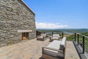 Stone exterior with an integrated outdoor fireplace, expansive paver patio, and cable railing system