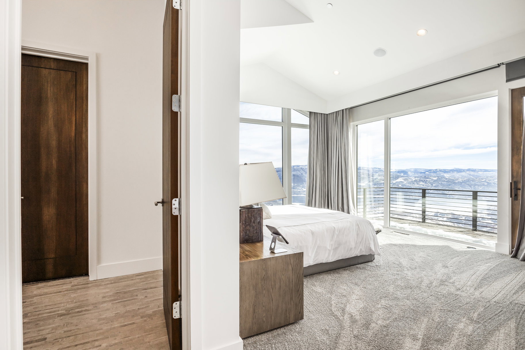 Expansive bedroom with vaulted ceilings, recessed lighting, and a large window wall overlooking a mountainous landscape