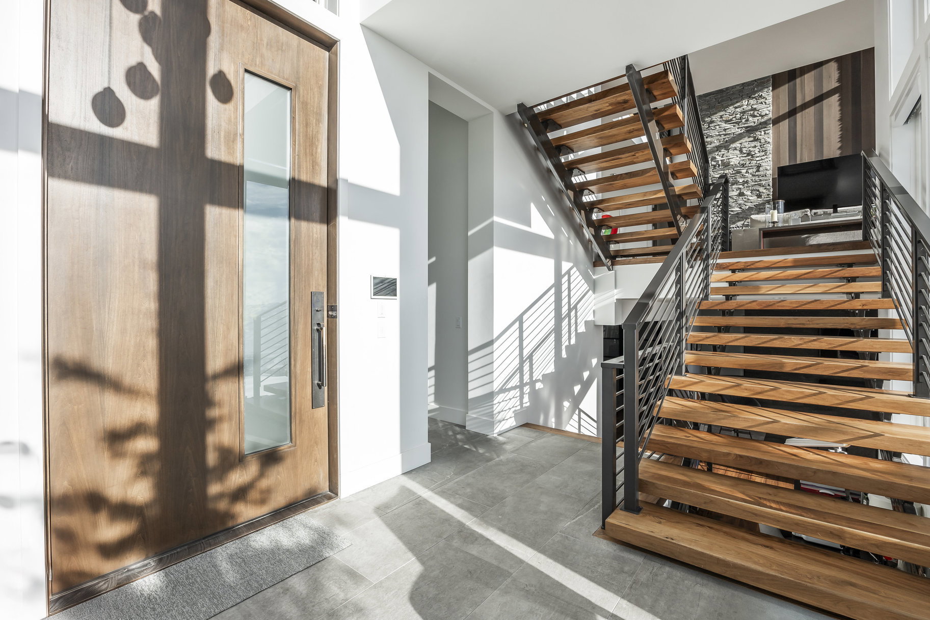 Entryway featuring a wood-panel door with a vertical glass insert, a modern dark-finish handle, and grey tile flooring