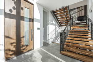 Entryway featuring a wood-panel door with a vertical glass insert, a modern dark-finish handle, and grey tile flooring