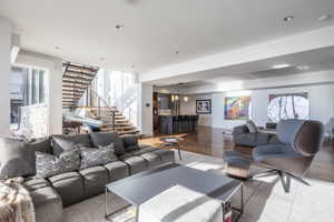 Open-concept living area featuring wood-finish flooring throughout, a modern floating staircase with metal railing, and recessed ceiling lighting
