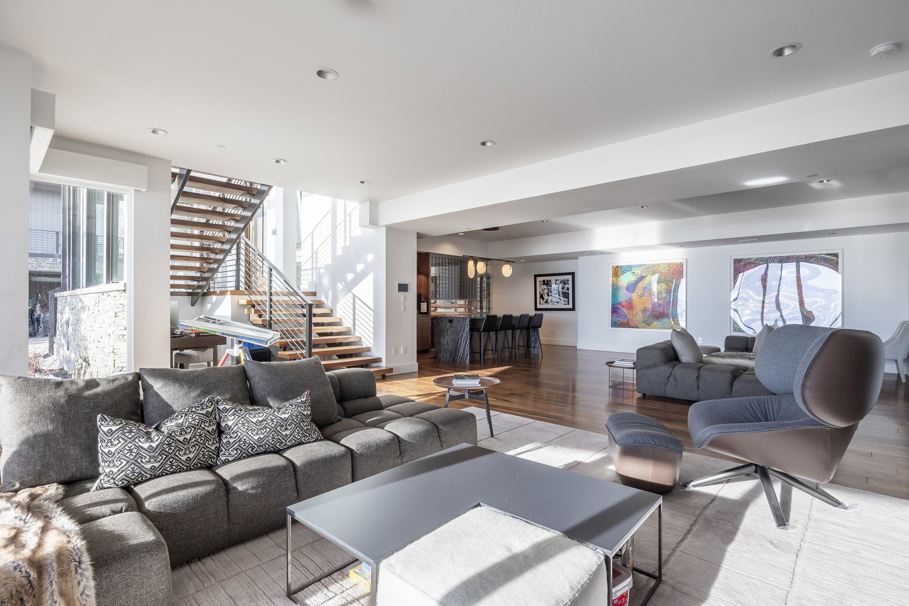 Open-concept living area featuring wood-finish flooring, a contemporary staircase with metal railings, recessed lighting, and a built-in bar area with pendant lighting